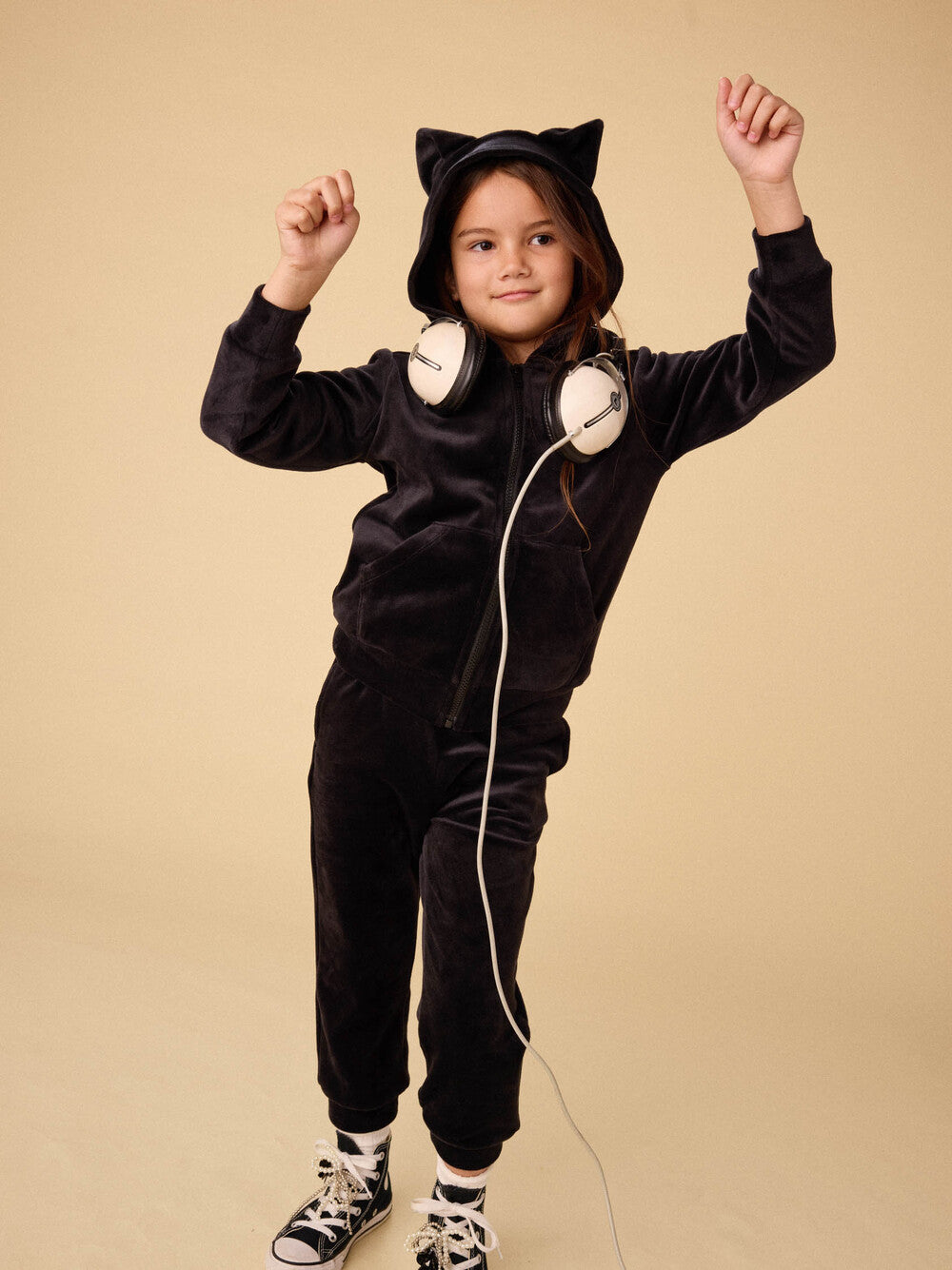 Child wearing a black cat-themed onesie with ears and a tail on a beige background