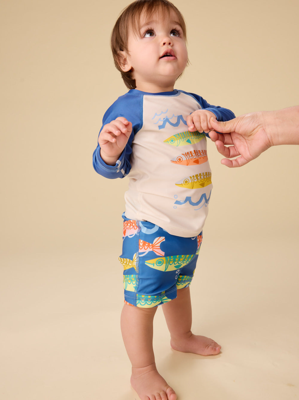 Child wearing a colorful shirt and shorts set with fish design on a beige background
