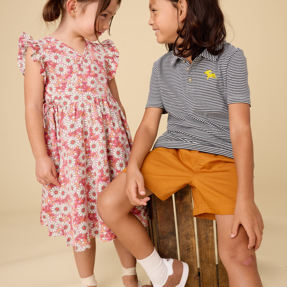 Two young girls in summer clothing sitting on a wooden crate against a beige background