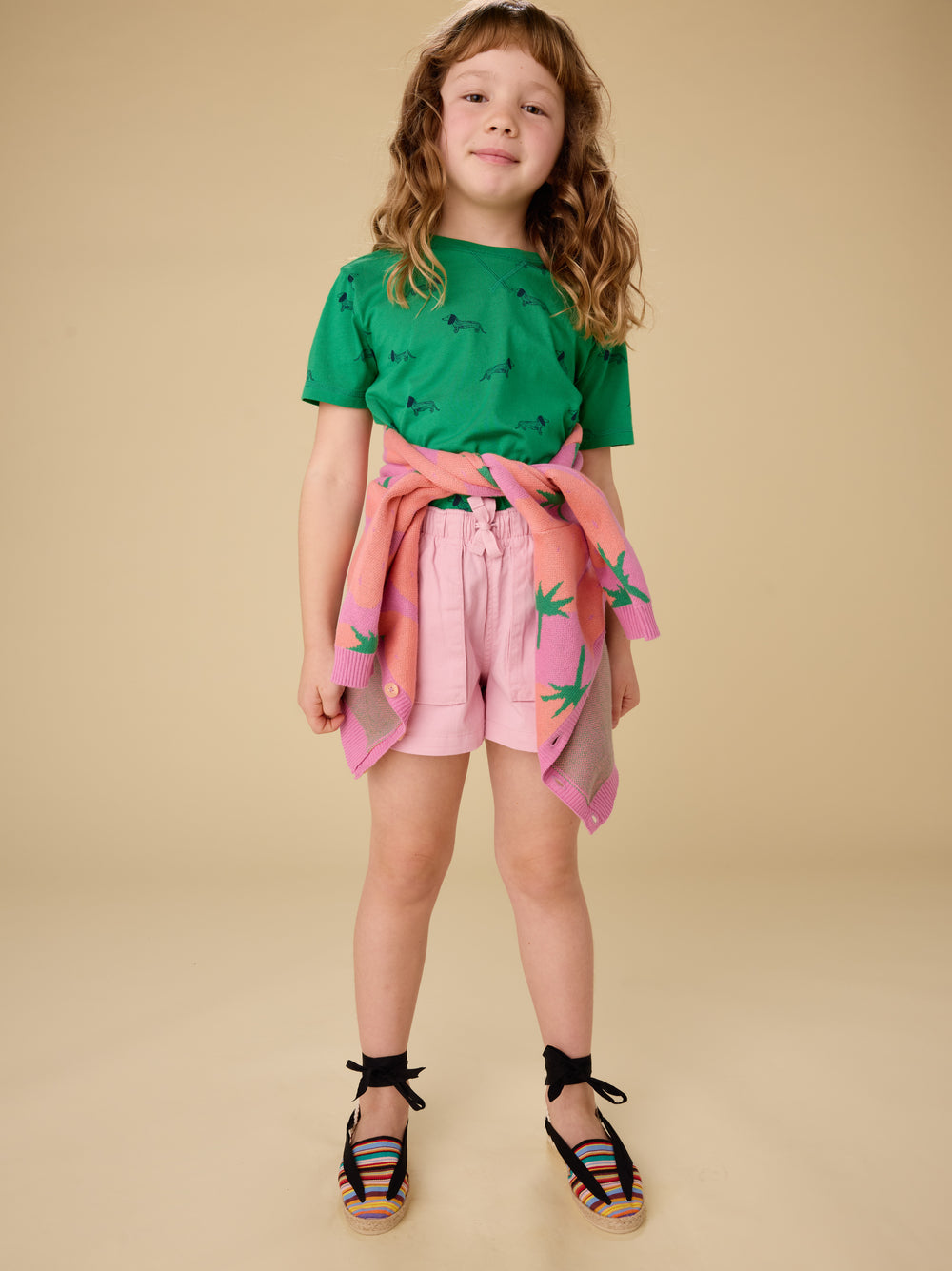 Young girl wearing a green top and pink shorts with a floral pattern on a beige background