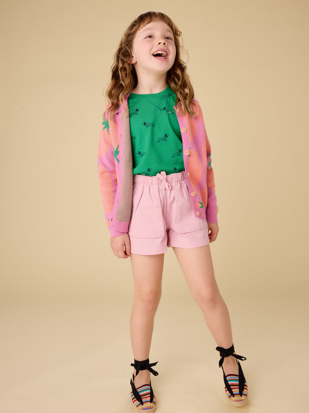Young girl in a green shirt and pink shorts with a colorful jacket on a beige background