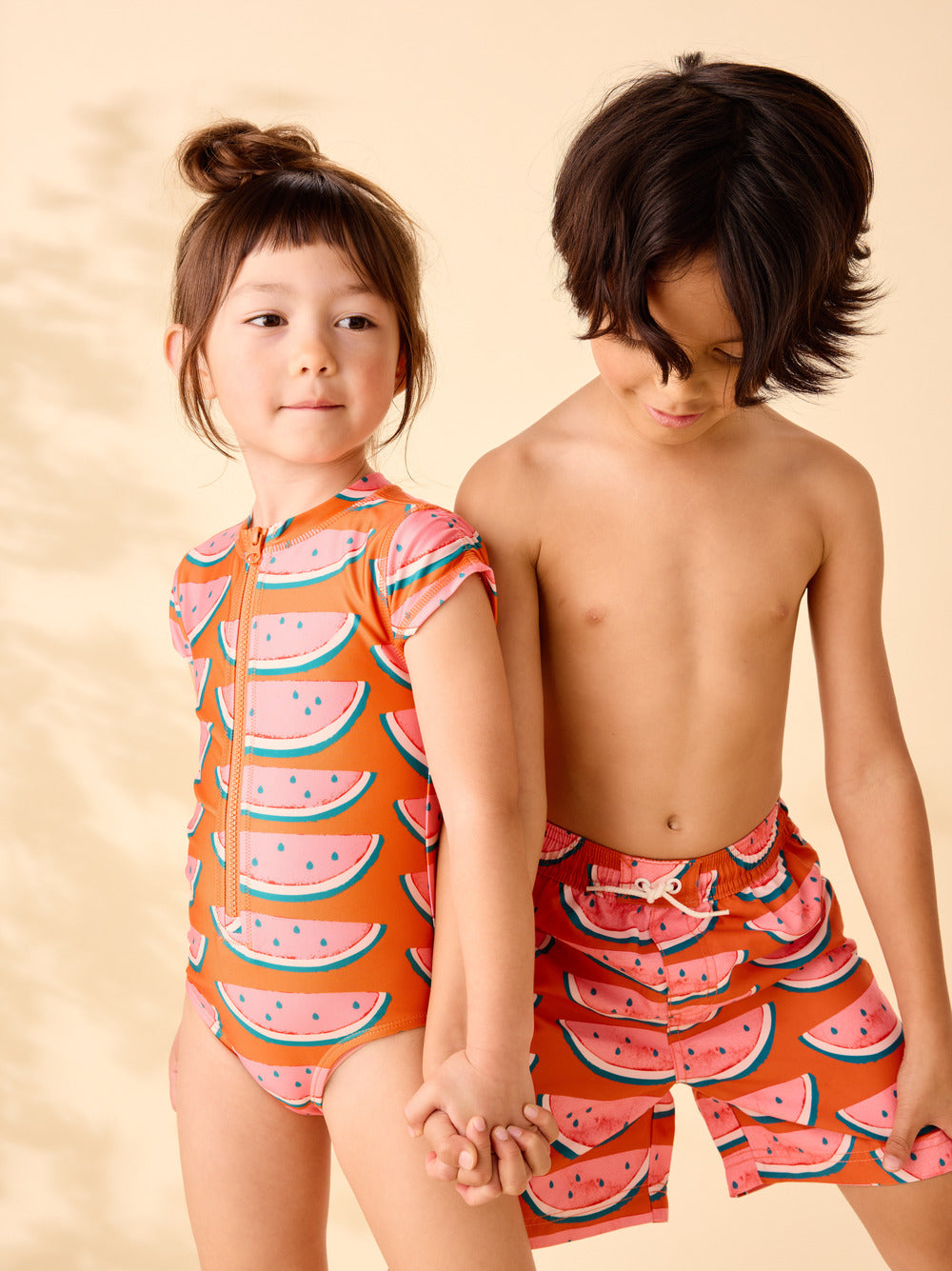 Two children wearing watermelon-themed swimwear on a beige background