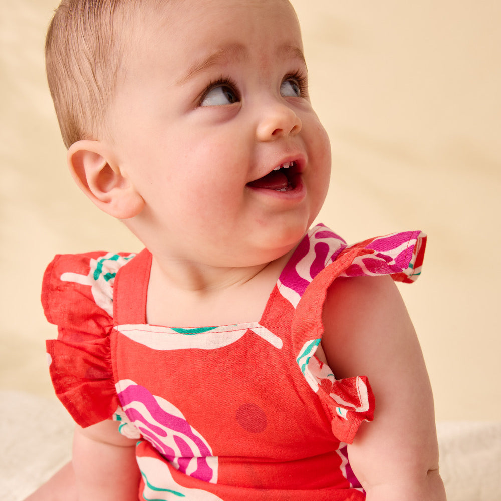 Baby wearing a red floral dress against a beige background