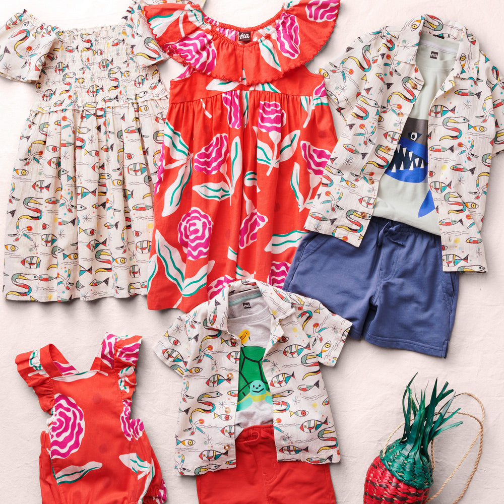 Collection of children's clothing including dresses, shirts, shorts, and a bag on a light background
