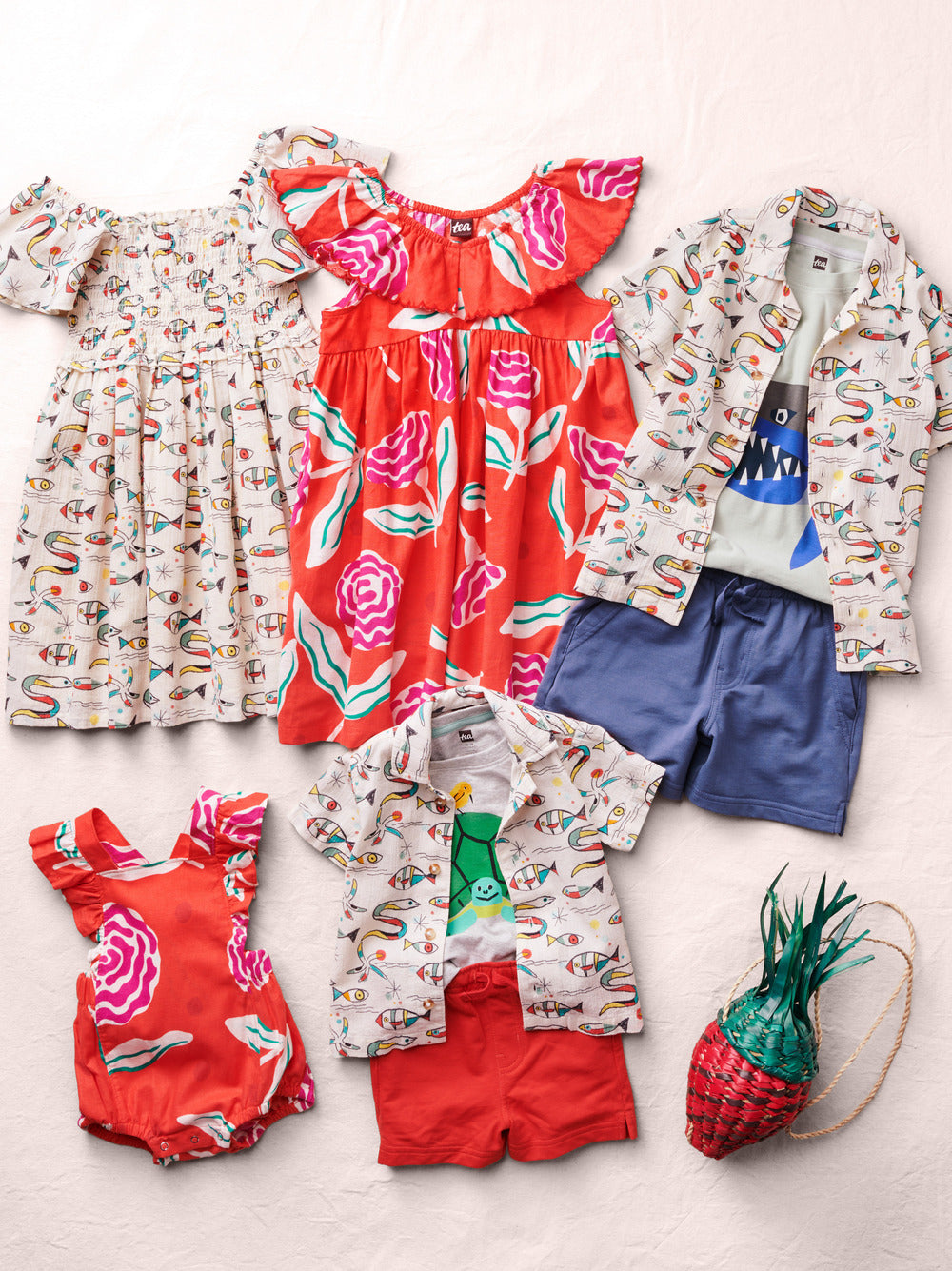 Collection of children's clothing including dresses, shirts, shorts, and a bag on a light background
