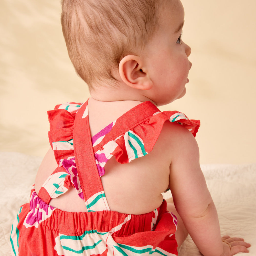 Baby wearing a colorful dress sitting on a beige surface