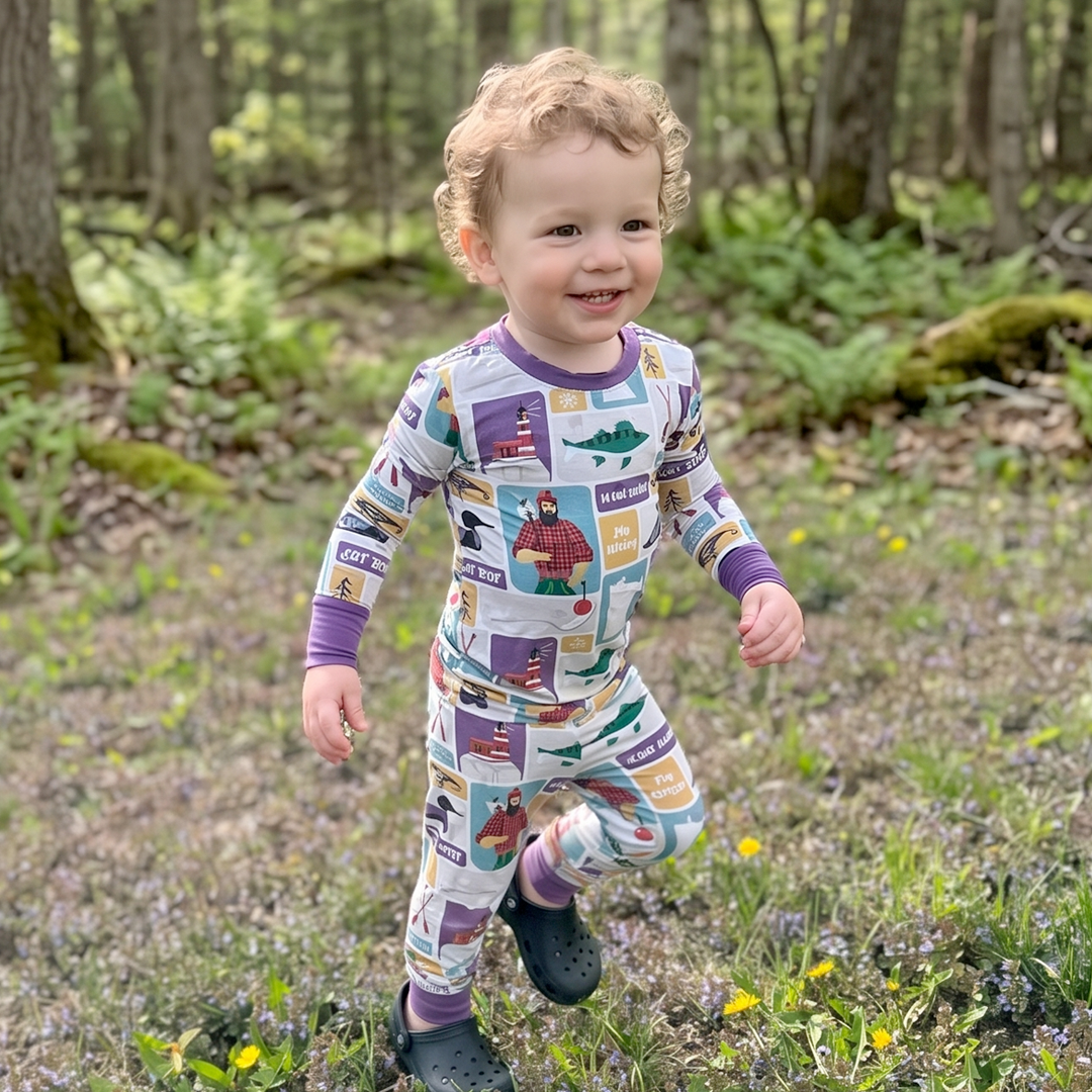 Child wearing a colorful onesie with a map design, standing in a forest.