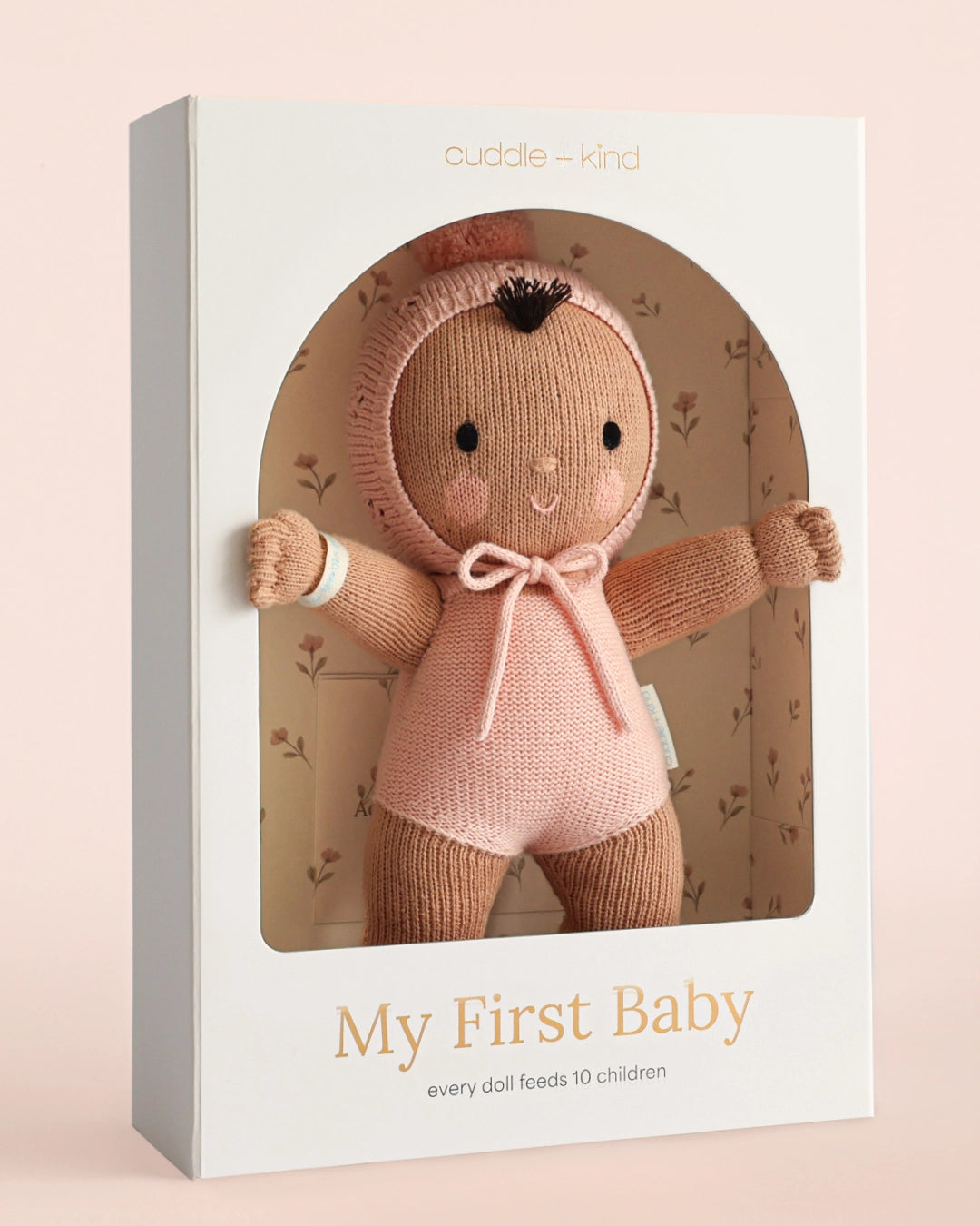 Cuddle + Kind doll in packaging with 'My First Baby' text on a pink background
