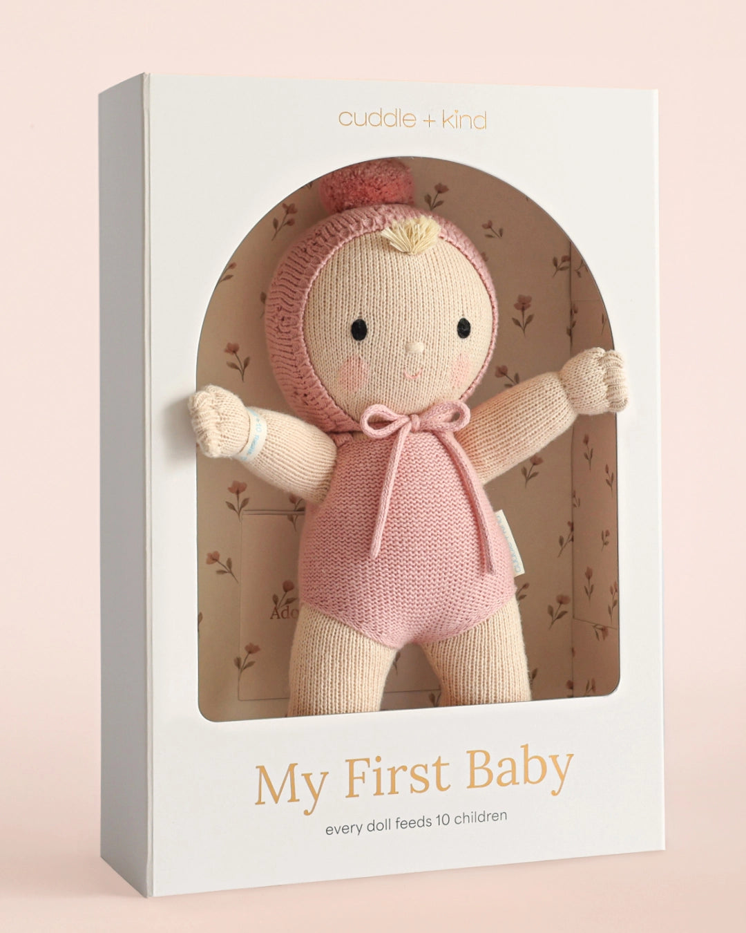 Cuddle + Kind doll in packaging with 'My First Baby' text on a pink background
