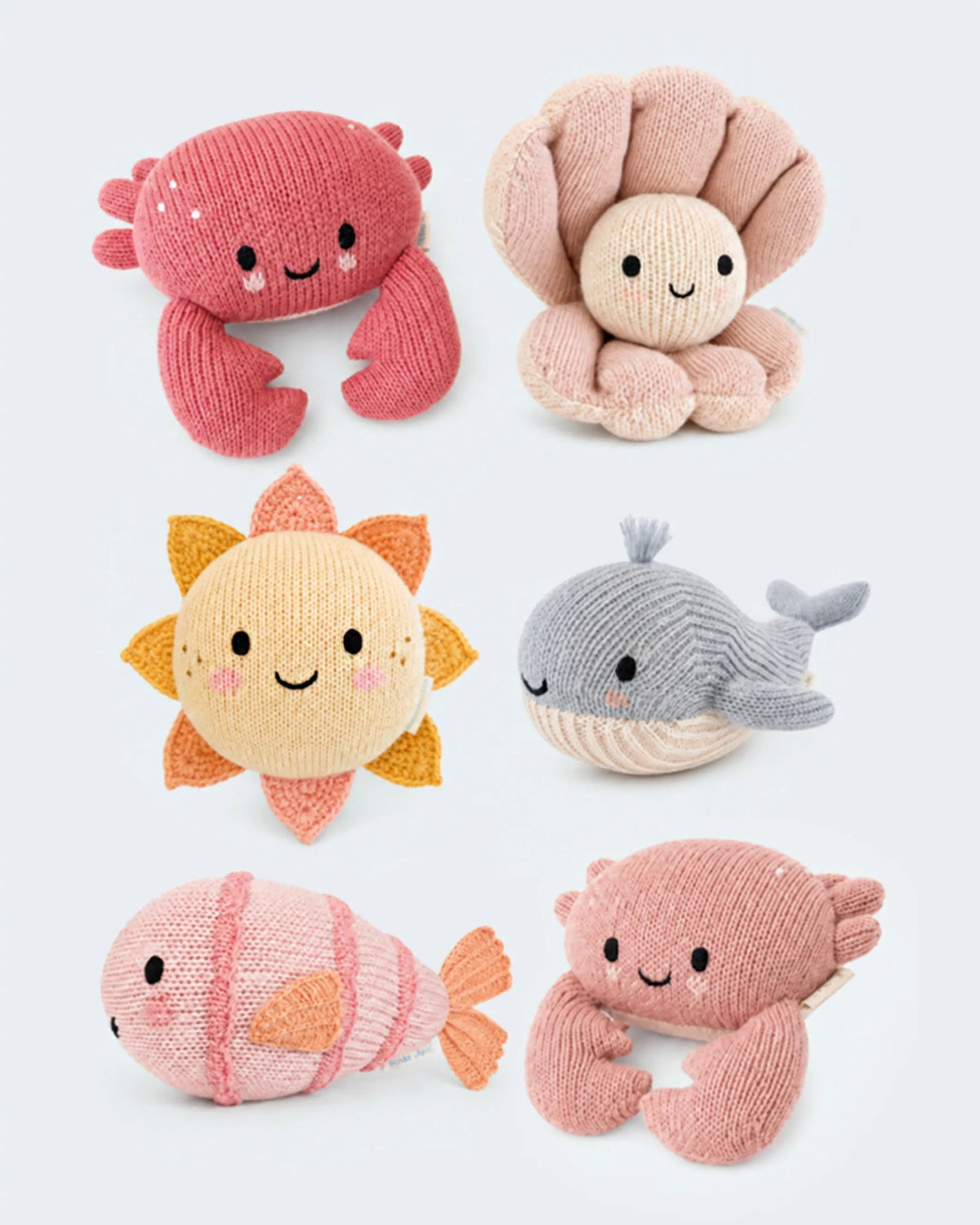 Six knitted plush toys arranged on a light gray background: a pink crab, a beige octopus, a yellow sun, a gray whale, a pink fish, and a pink crab.