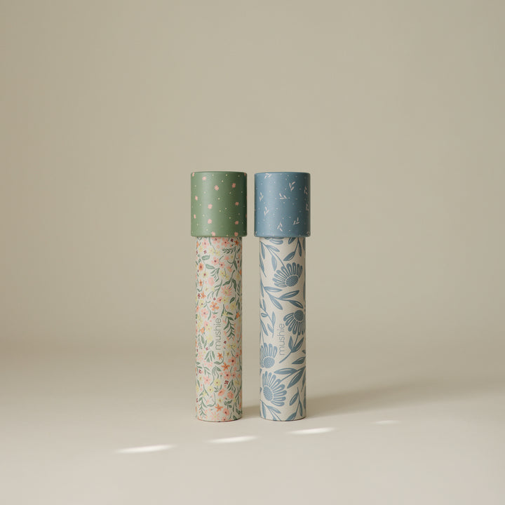 Two Mushie paper kaleidoscopes standing vertically against a light background, featuring the Floral Combo pattern with green caps and botanical floral illustrations.