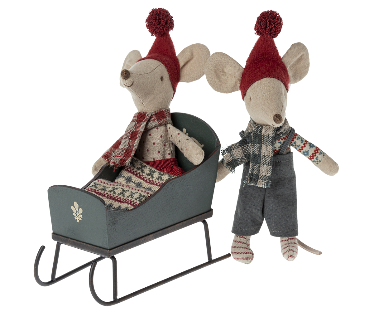 Two Maileg mouse plush toys with winter clothing—one seated inside a green wooden toy sleigh and the other standing beside it against a transparent background.