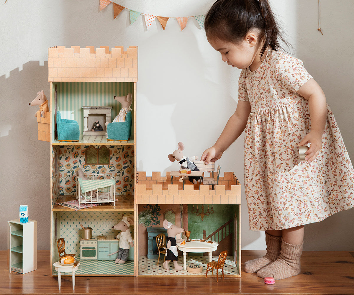 Child playing with a wooden dollhouse set in a room.