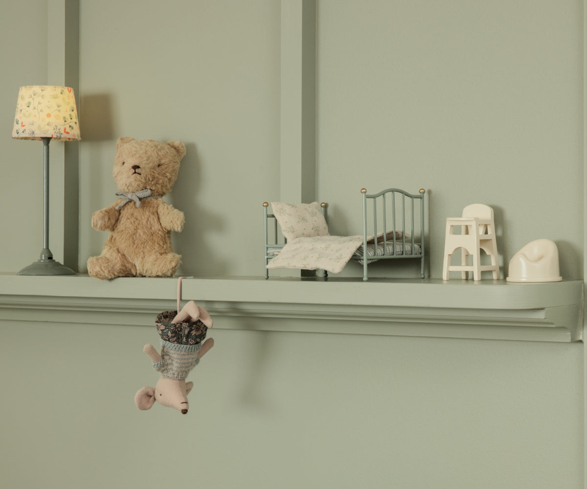 Decorative shelf with teddy bear, small bed, and lamp against a green wall