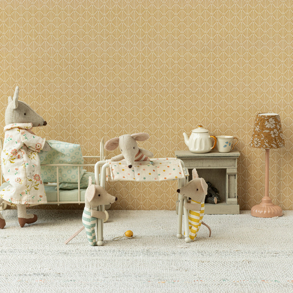 Maileg miniature nursery scene featuring a standing adult mouse in a floral nightgown next to a white metal baby crib, with a baby mouse sleeping on a changing table, a small elephant toy, a teapot on a fireplace mantle, and a floral floor lamp.