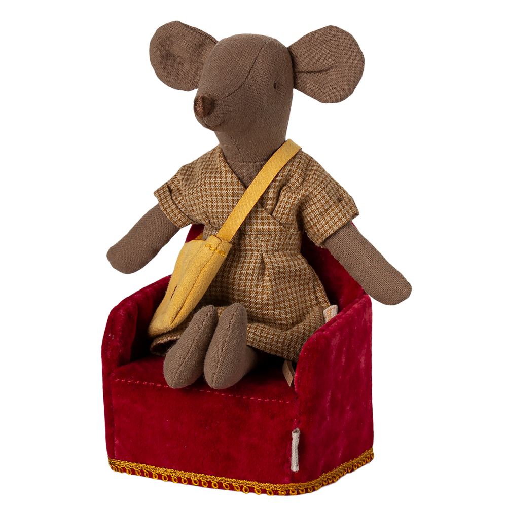 A Maileg mouse dressed in a plaid dress and yellow sash, sitting comfortably in a miniature red velvet armchair.