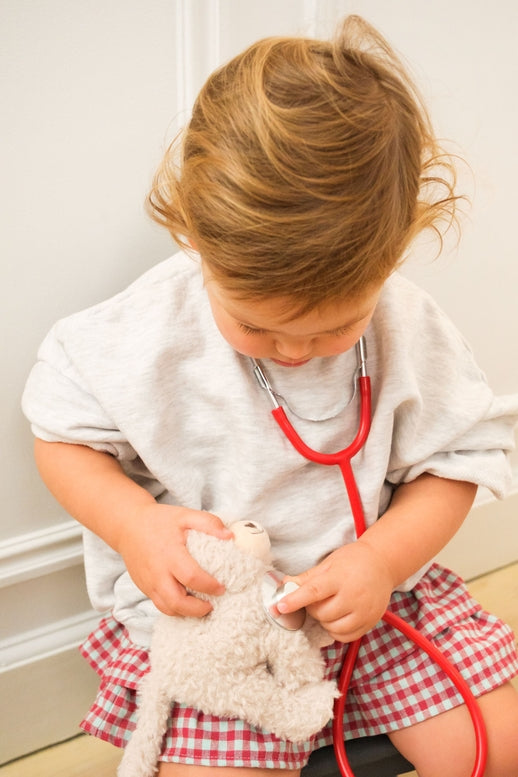 Child playing with a teddy bear and stethoscope in a room.