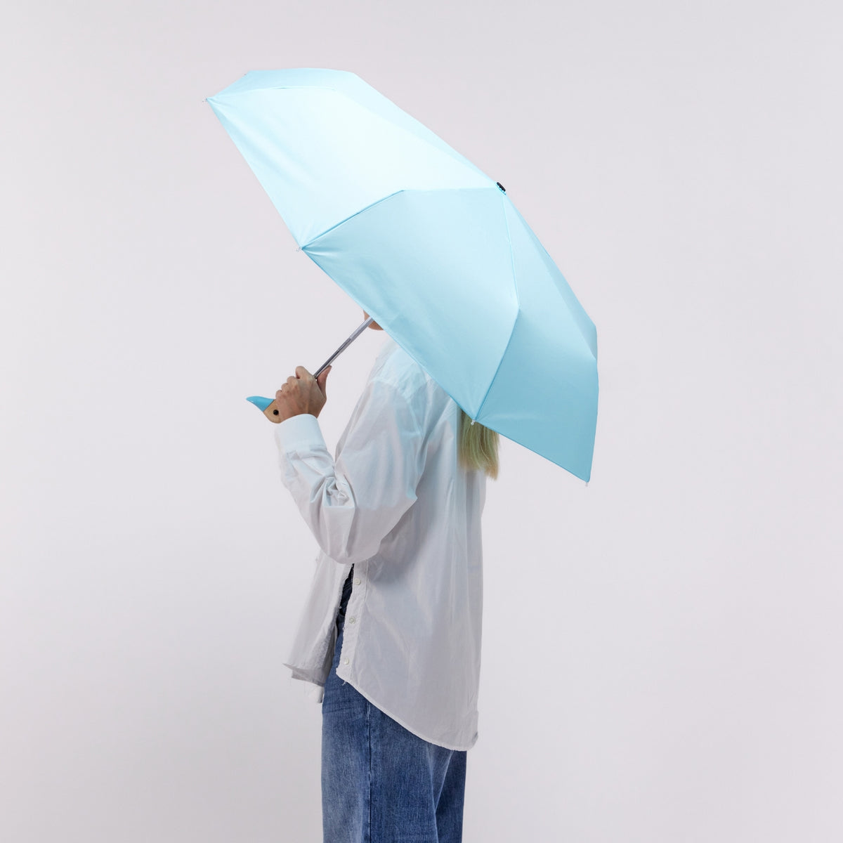 Person holding a light blue umbrella against a plain background