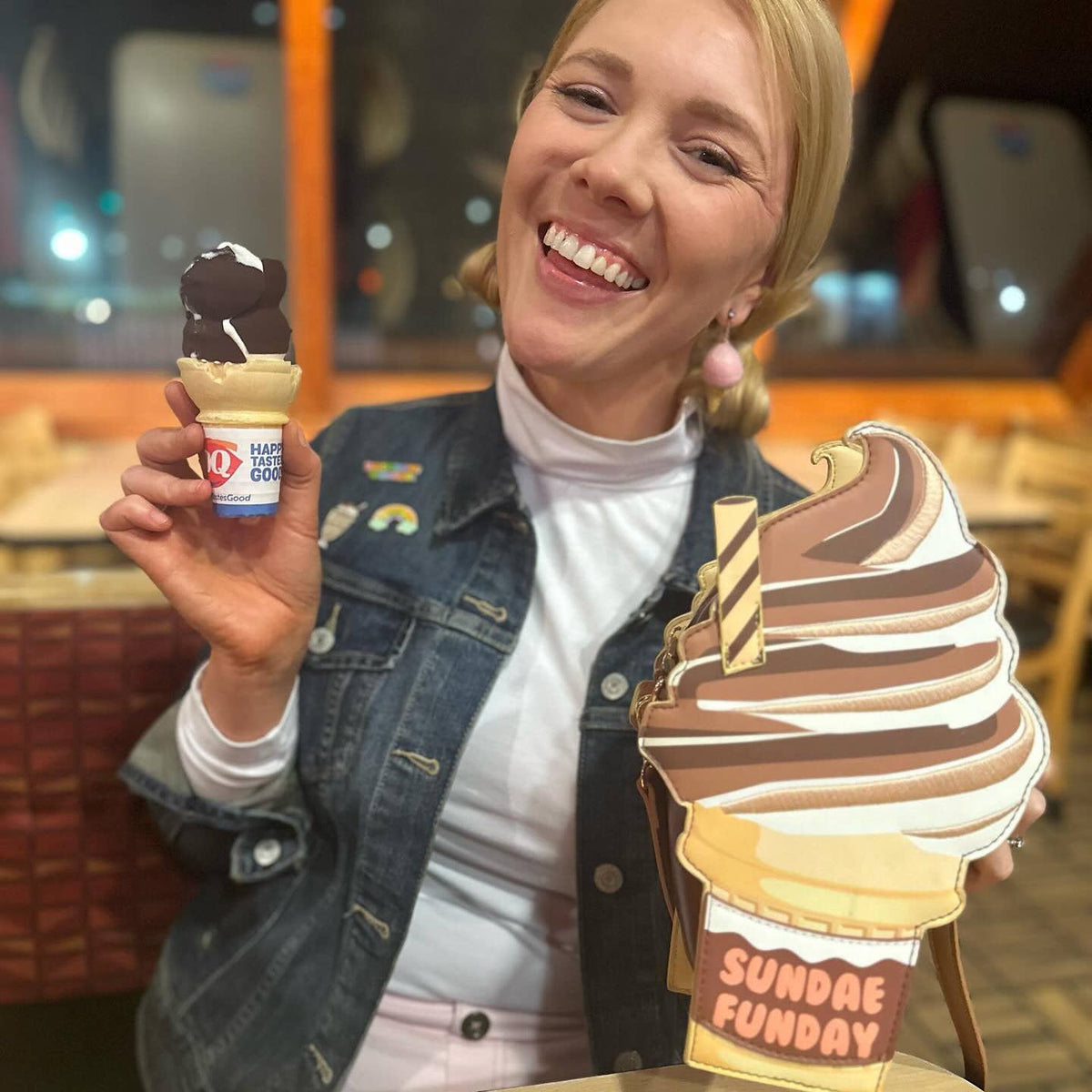 Person holding a small ice cream cone with a large cardboard ice cream cone labeled 'Sundae Funday' in a casual setting.