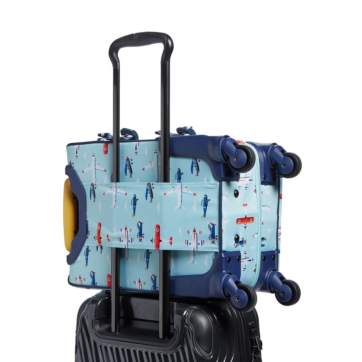 Rear three-quarters view of a light blue State Bags Mini Logan carry-on suitcase featuring an all-over airplane pattern, a black telescopic handle, 360-degree spinner wheels, and dark blue trim details against a transparent background.