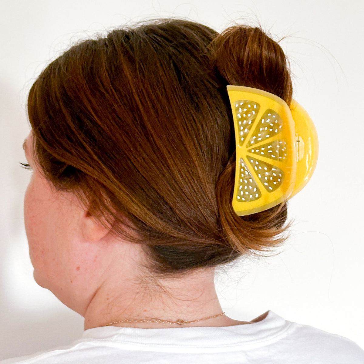 Person with a yellow lemon-shaped hair clip in their hair against a white background