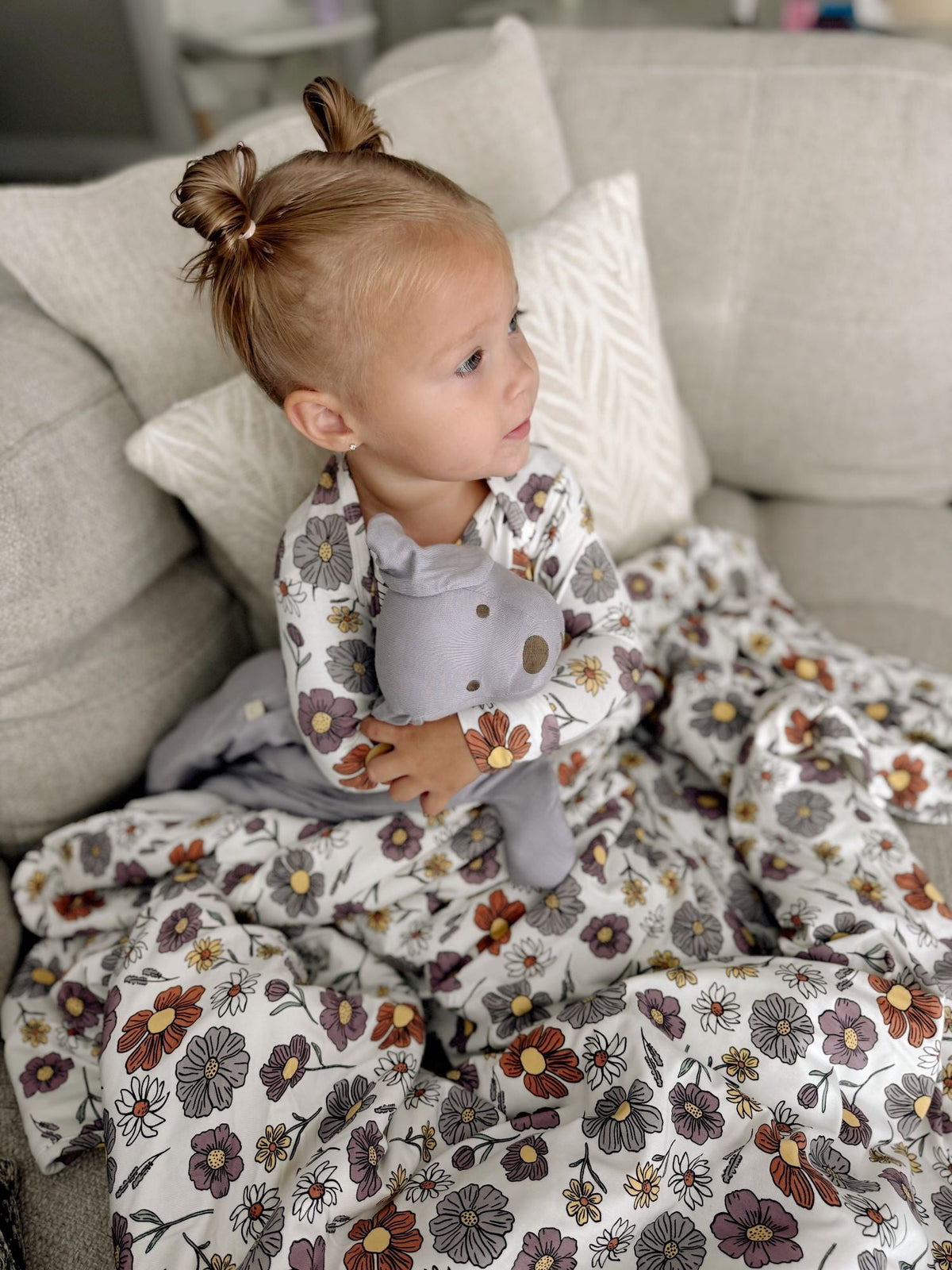 Child sitting on a couch with a floral blanket, wearing a patterned outfit.