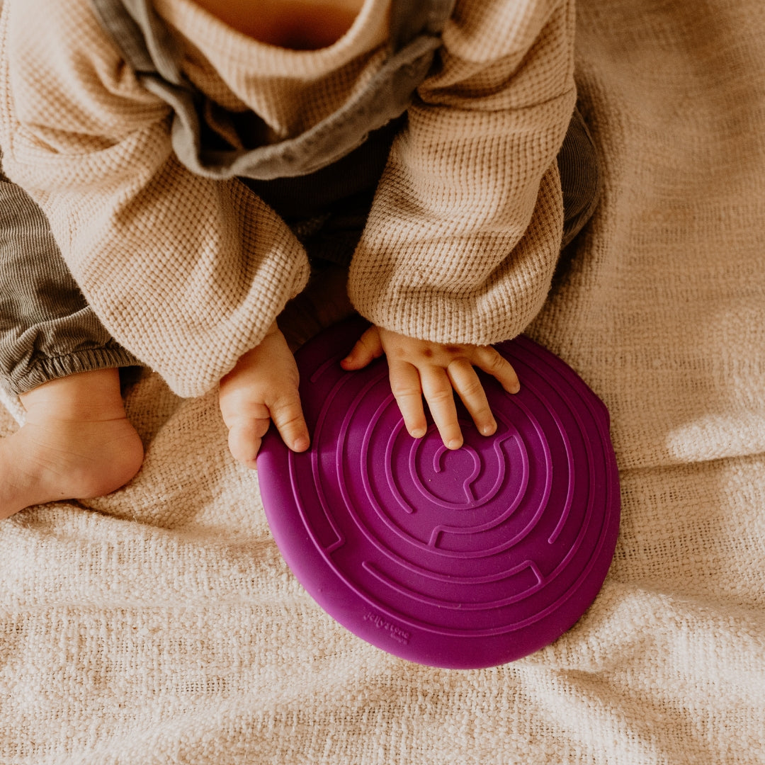 Child's hands holding a purple lid on a beige blanket
