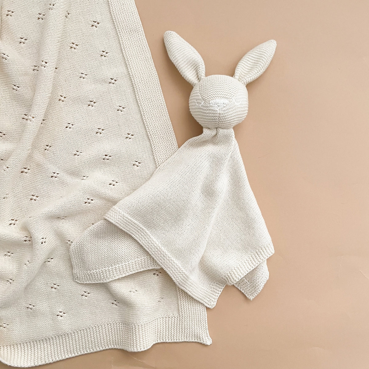 White knitted bunny comfort toy on a beige blanket against a beige background