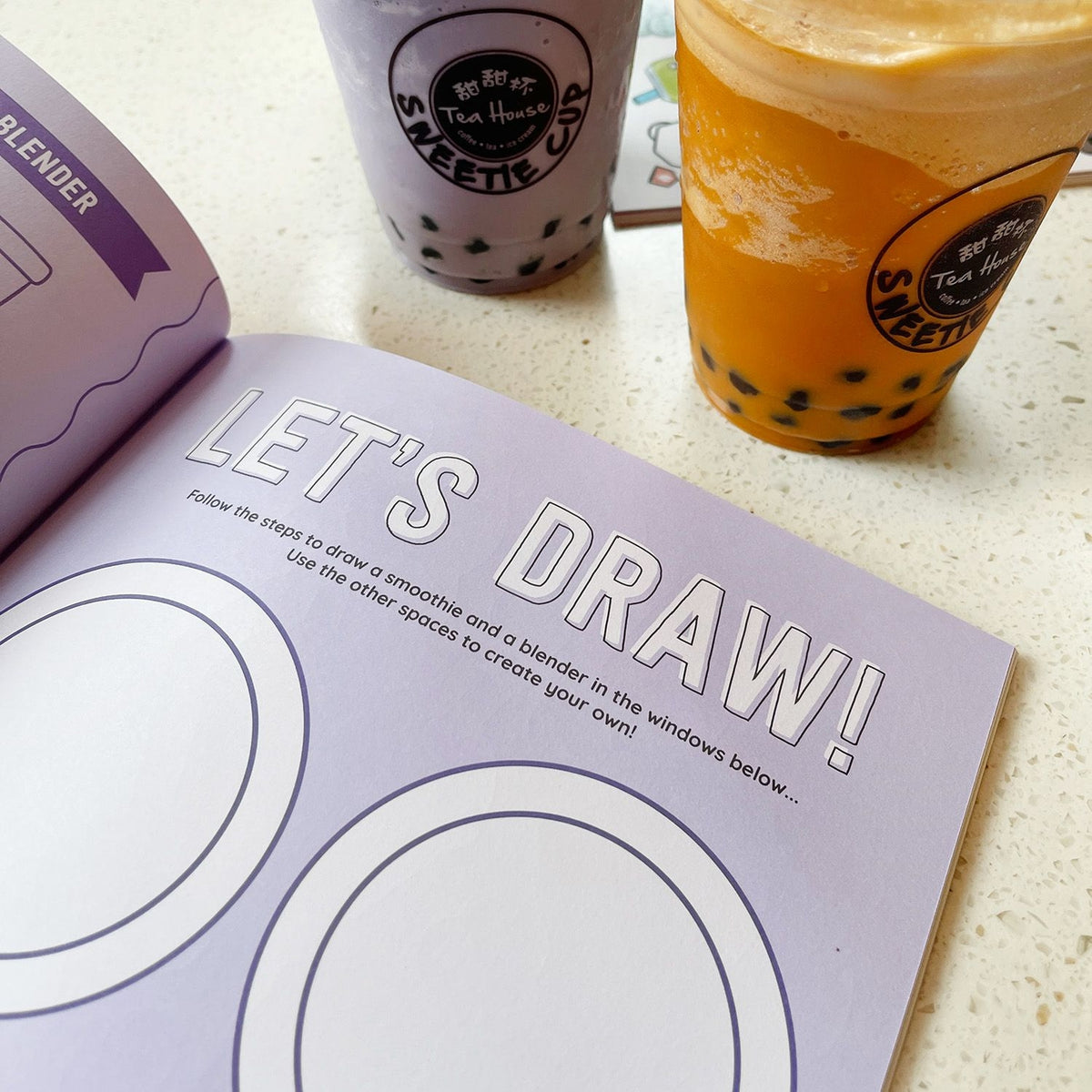 Book with drawing instructions next to bubble tea drinks.