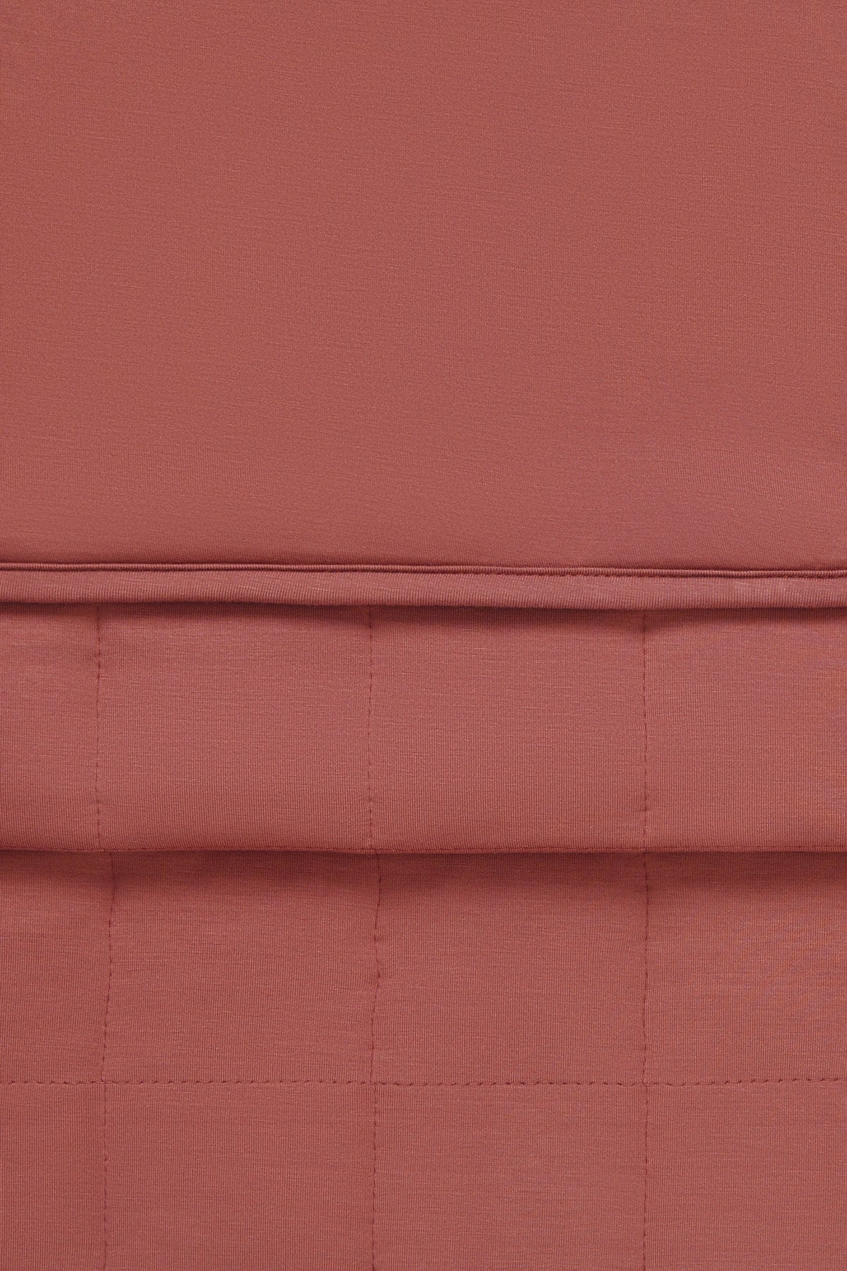 A close-up of a warm colored fabric napkin with a quilted grid pattern and a horizontal stitched seam.