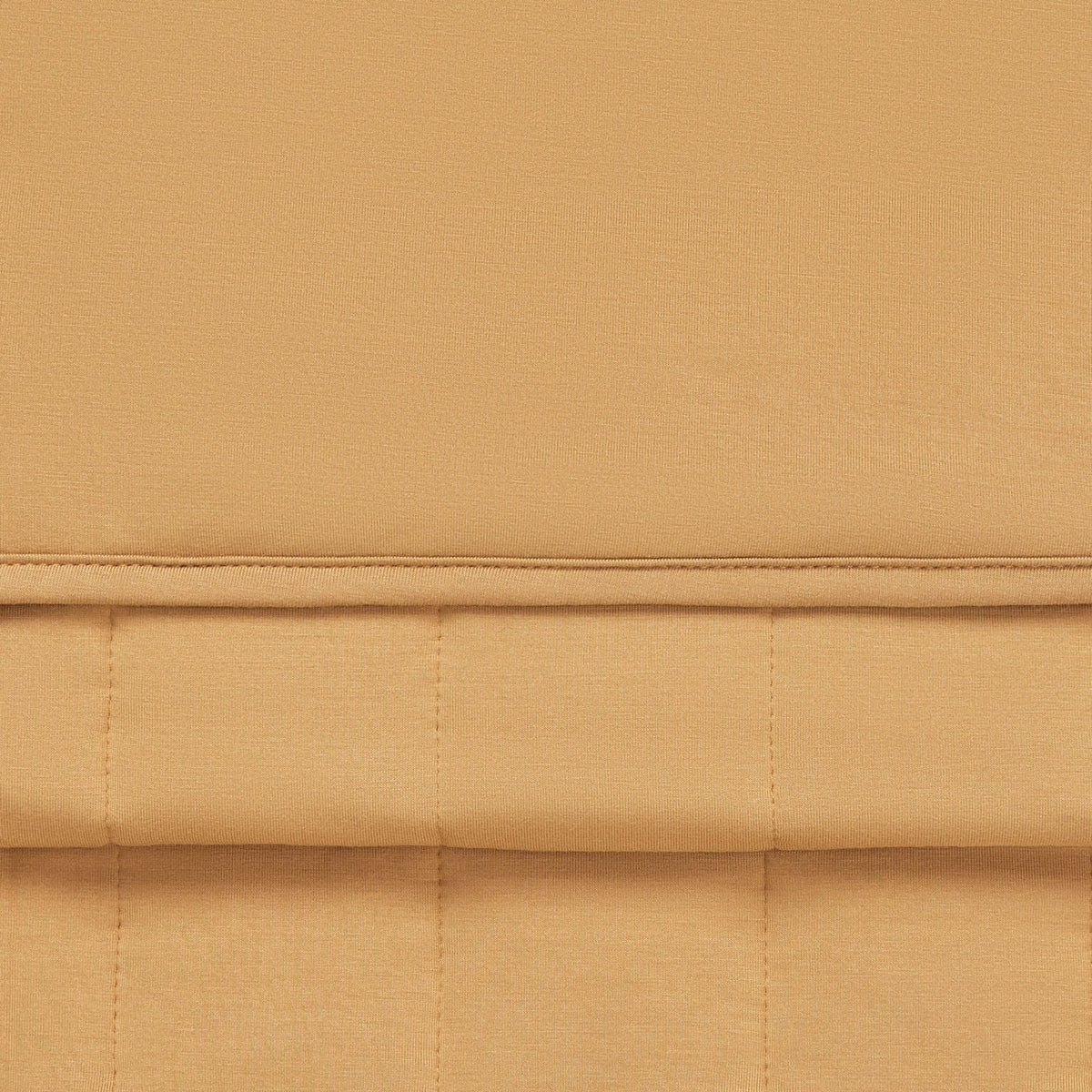 A close-up of a warm tan or camel-colored fabric with a quilted grid pattern and a horizontal stitched seam.