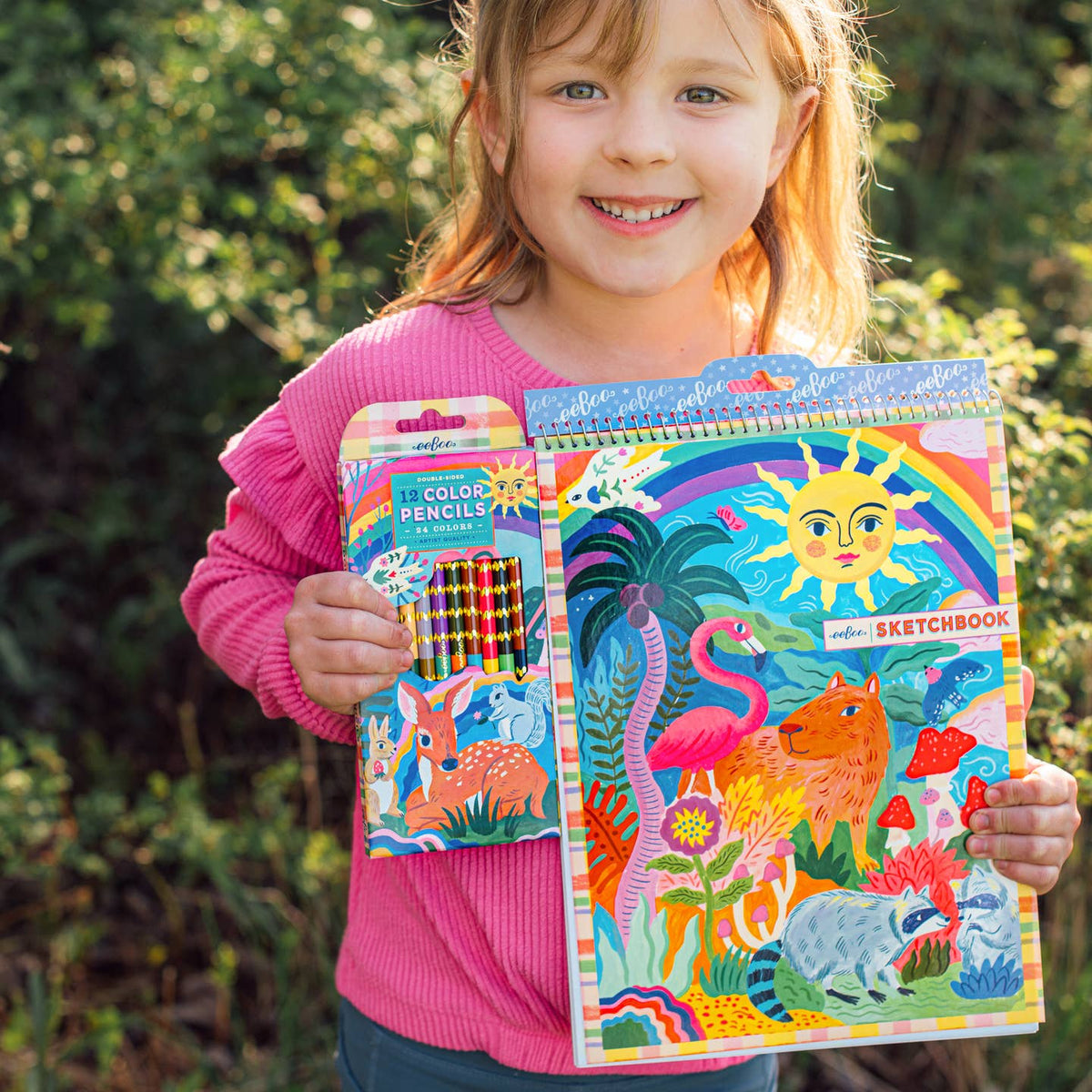 Child holding a colorful sketchbook and coloring book with nature-themed designs.