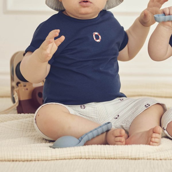 Baby wearing a navy blue shirt and white shorts with a pattern, sitting on a beige surface.