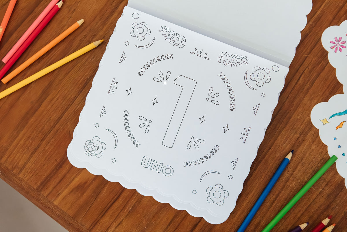 A white scalloped children's coloring book or activity sheet with the number 1 and the word UNO, photographed on a wooden table with colored pencils around it.