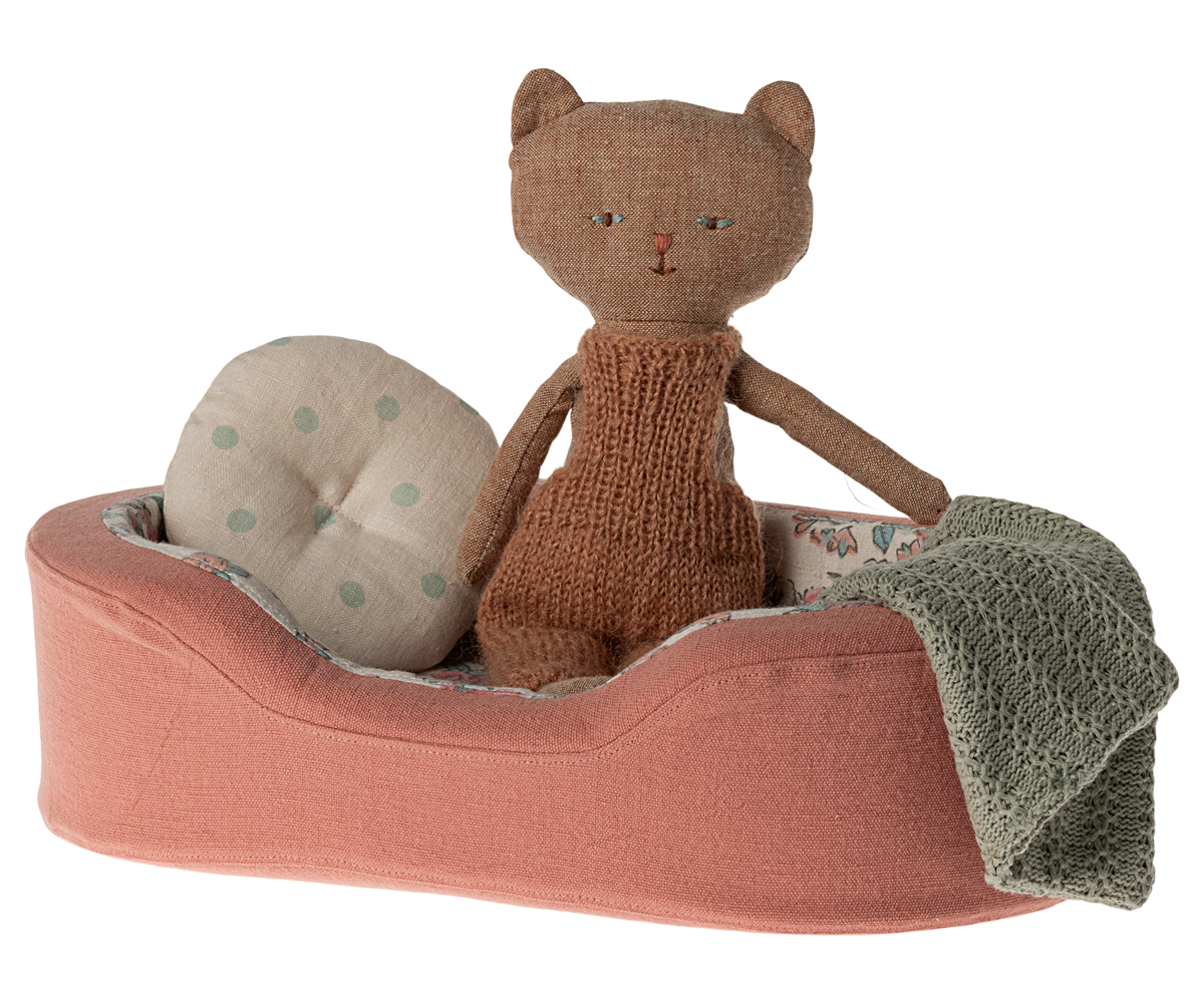 Knitted cat toy on a pink cushion with a blanket and polka dot pillow on a white background