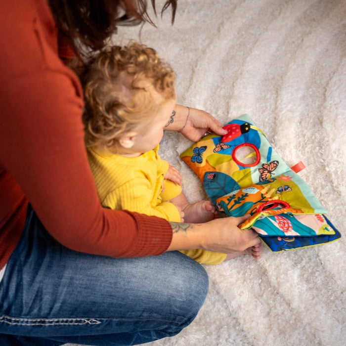 Person and child interacting with a colorful soft book on a textured surface