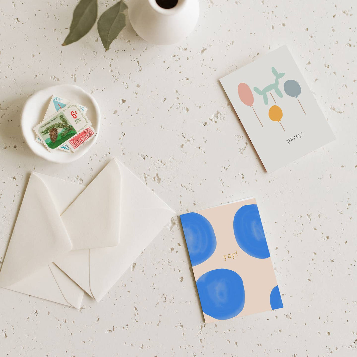 Stationery items including cards, an envelope, and a small dish with stamps on a light surface.