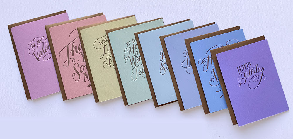 A set of colorful greeting cards arranged in a fan shape on a light background. The cards feature elegant metallic foil script text such as 'Happy Birthday' and 'The Best Years Come Soon.