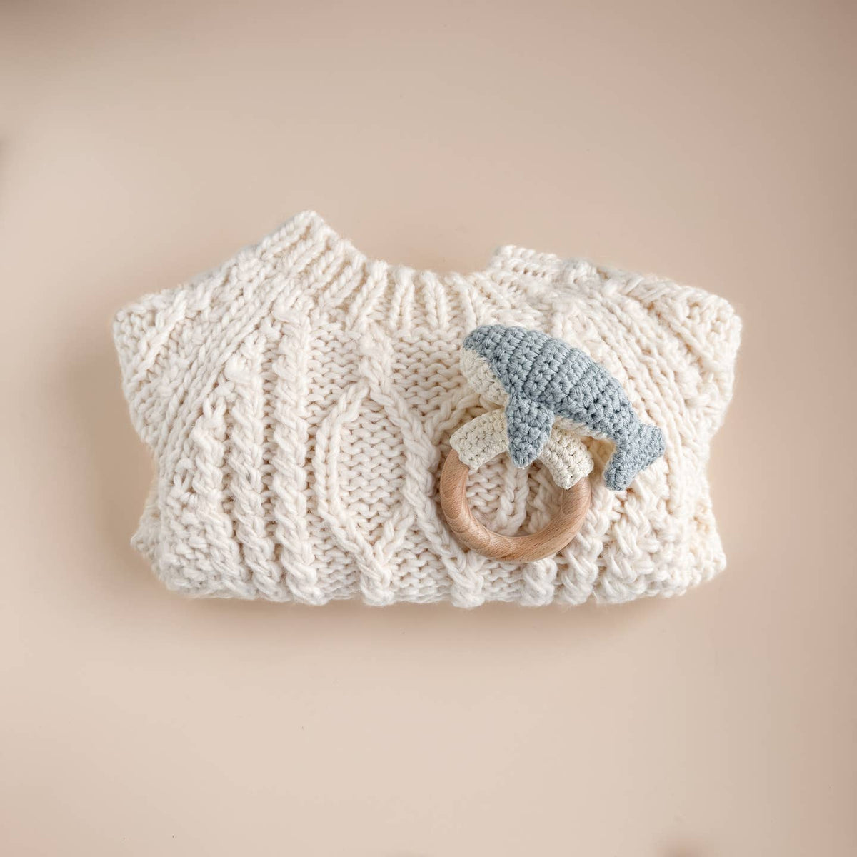 Knitted baby blanket with a wooden teething ring and blue toy on a beige background