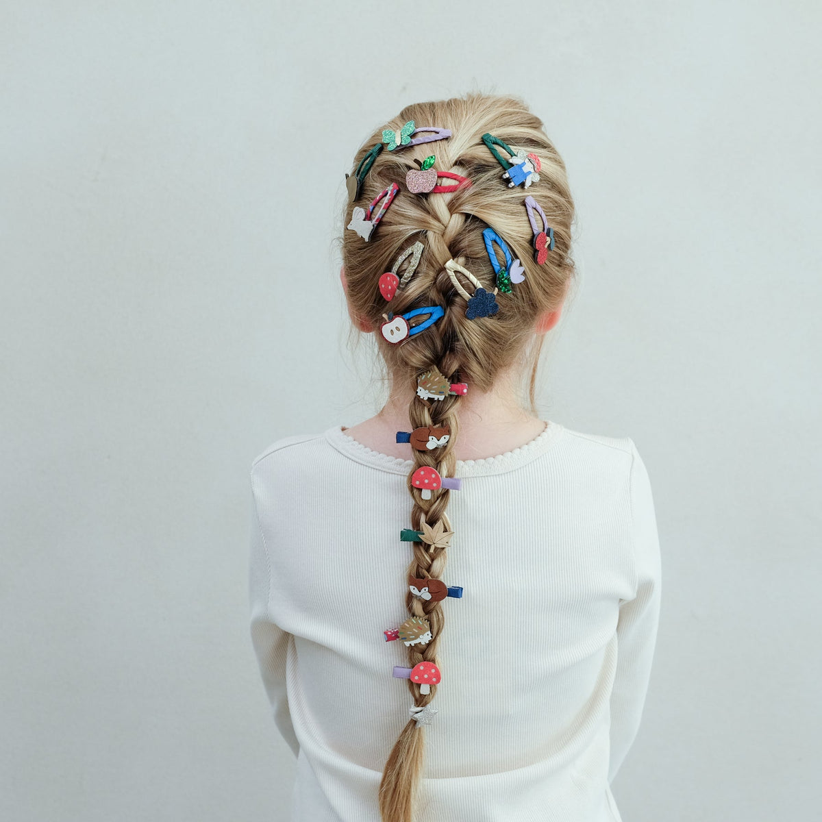 Person with braided hair adorned with colorful hair clips on a plain background