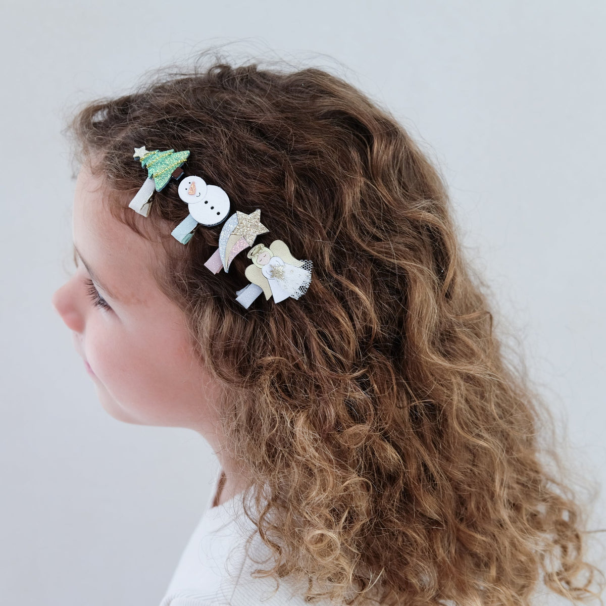 Child with curly hair wearing colorful hair clips on a plain background