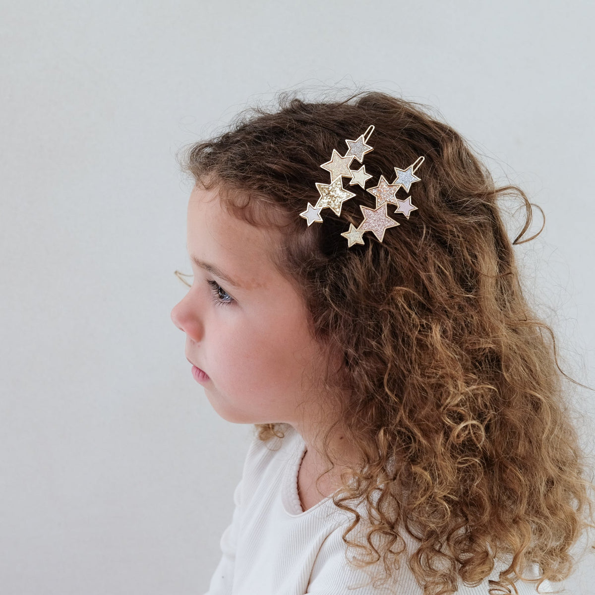A girl wearing a set of star-shaped hair clips in various colors on a white background