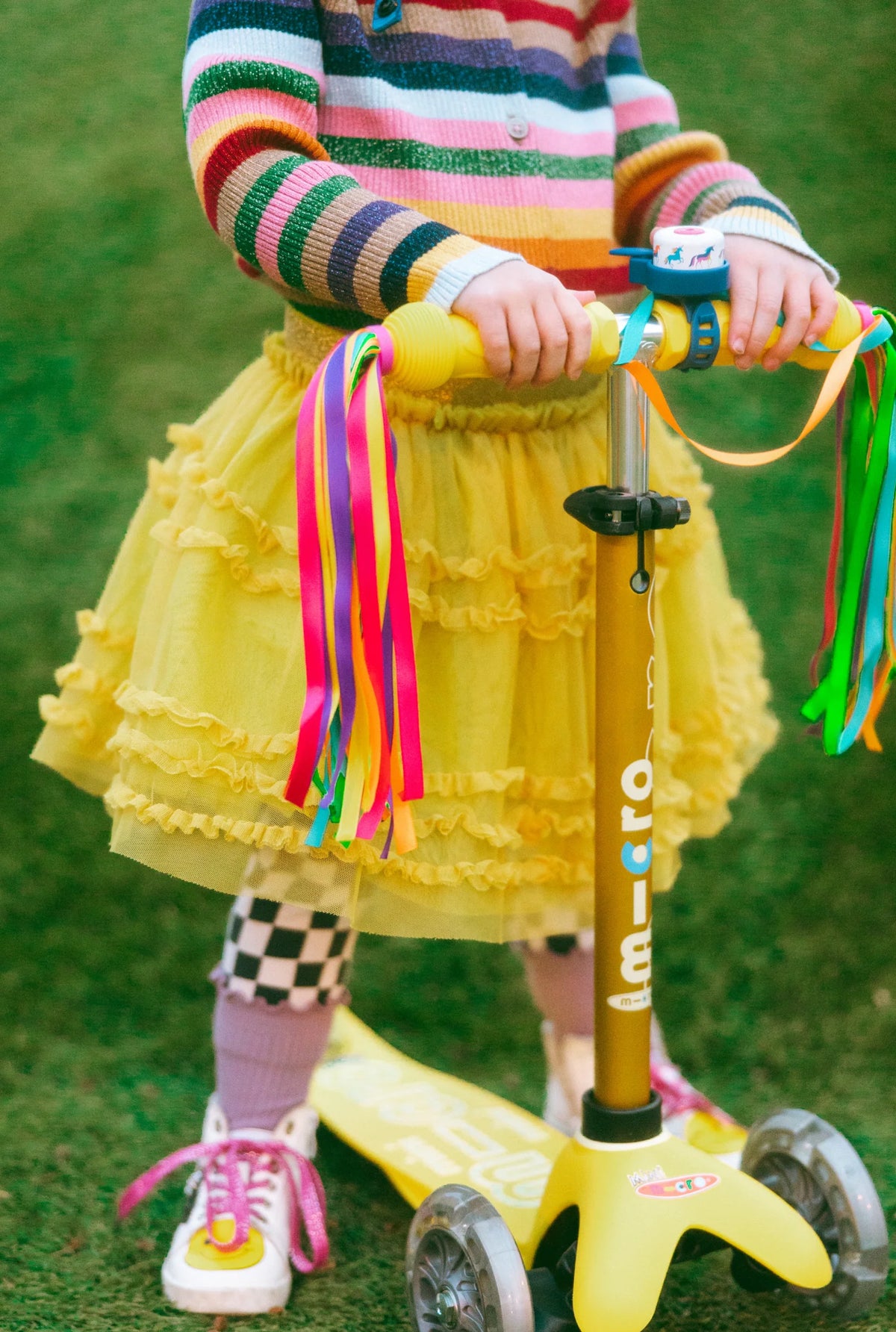Child on a yellow scooter with colorful ribbons, wearing a striped shirt and yellow skirt.
