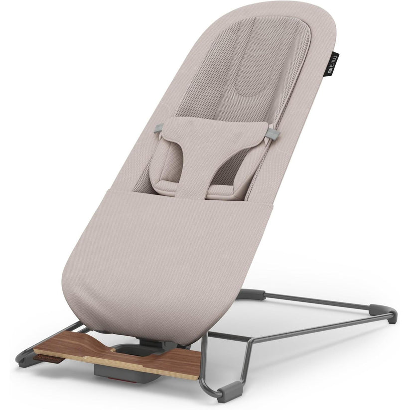 A baby bouncer chair with a light beige fabric cover and a dark gray metal stand, shown on a clean white background.