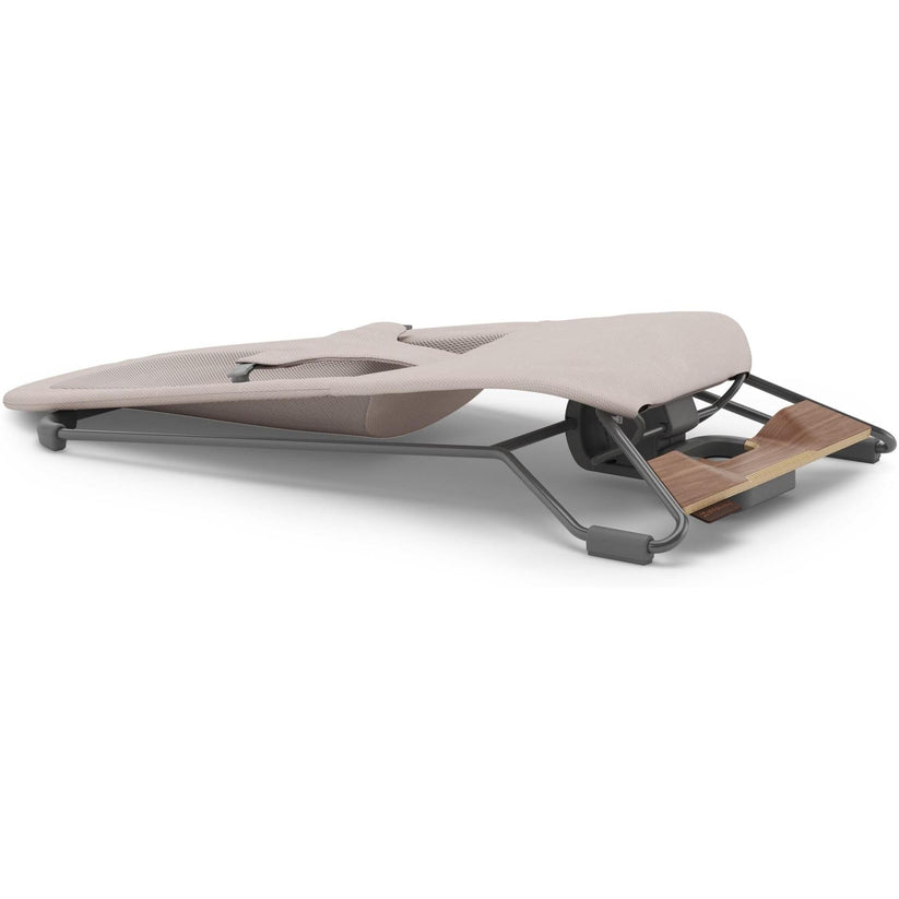 A modern adjustable exercise or massage table with a light beige cushioned top, dark gray metal frame, and a wooden footrest, shown on a plain white background.
