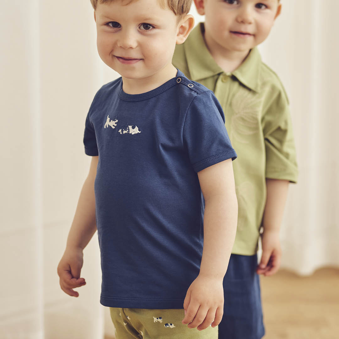 Two young boys wearing navy and green shirts with matching pants indoors.