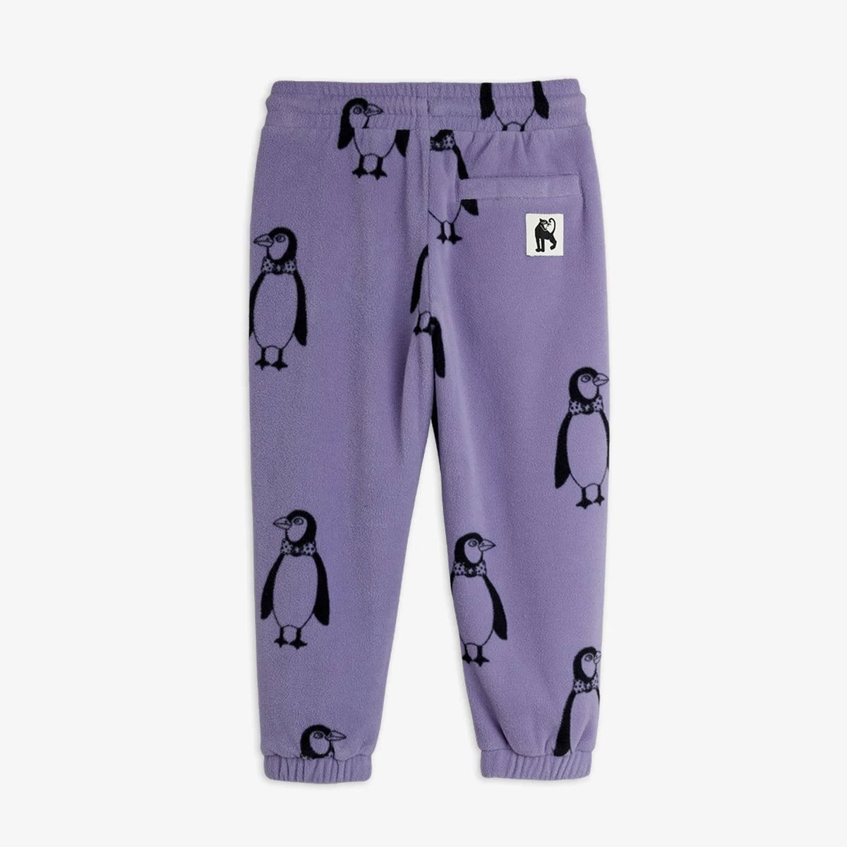 Purple sweatpants with an all-over penguin print, featuring a small white brand patch on the back pocket, photographed against a plain white background.