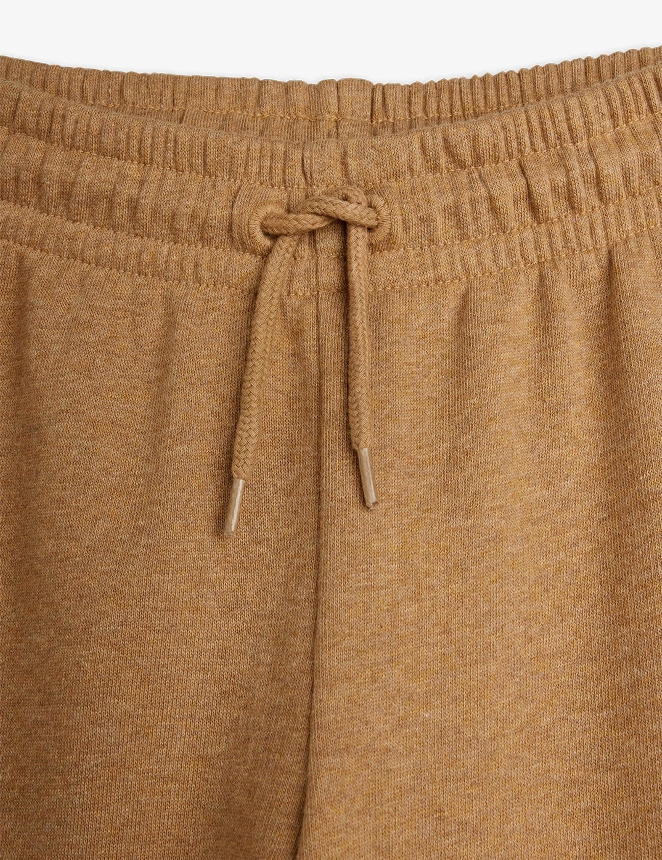 Close-up of a pair of knit lounge pants in a warm camel brown color, showing the elastic waistband and matching drawstring.