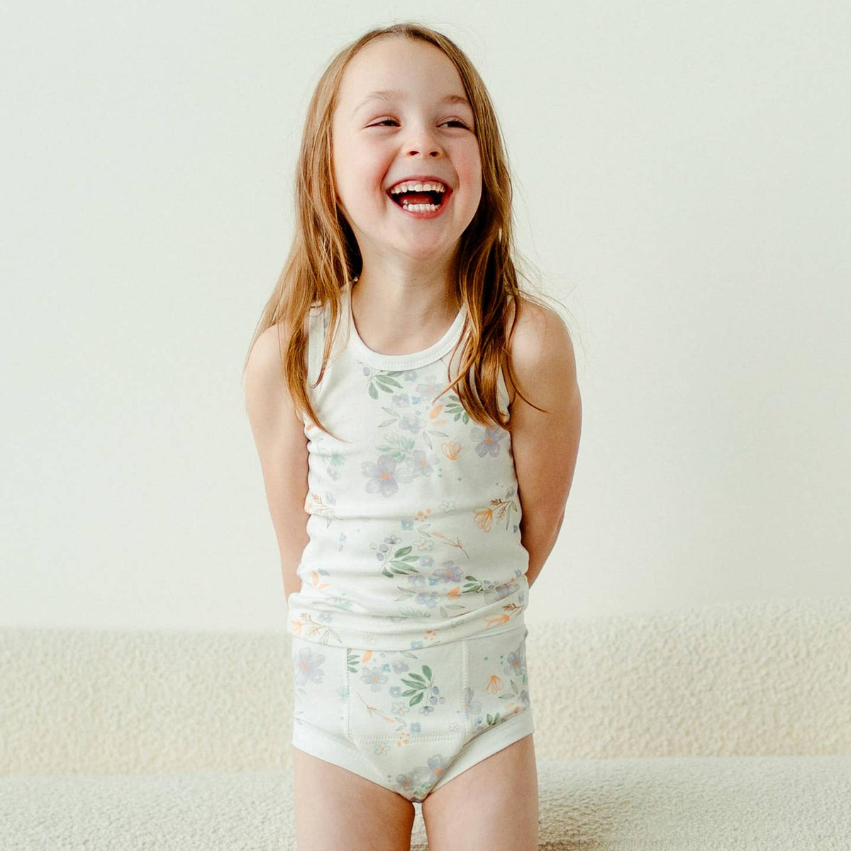 Young girl wearing a floral tank top and shorts on a plain background