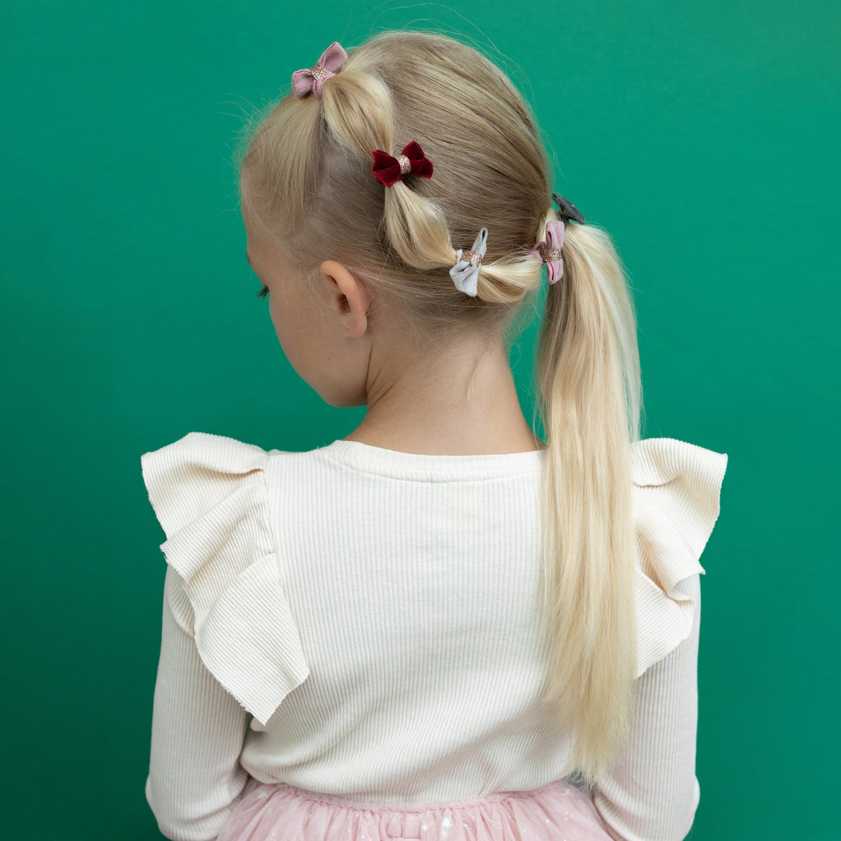 Child with styled hair and a white top on a green background